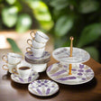 Ceramic tea set with cups, saucers, and a three-tiered stand on a wooden surface with a blurred green background.