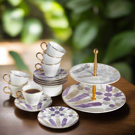 Ceramic tea set with cups, saucers, and a three-tiered stand on a wooden surface with a blurred green background.